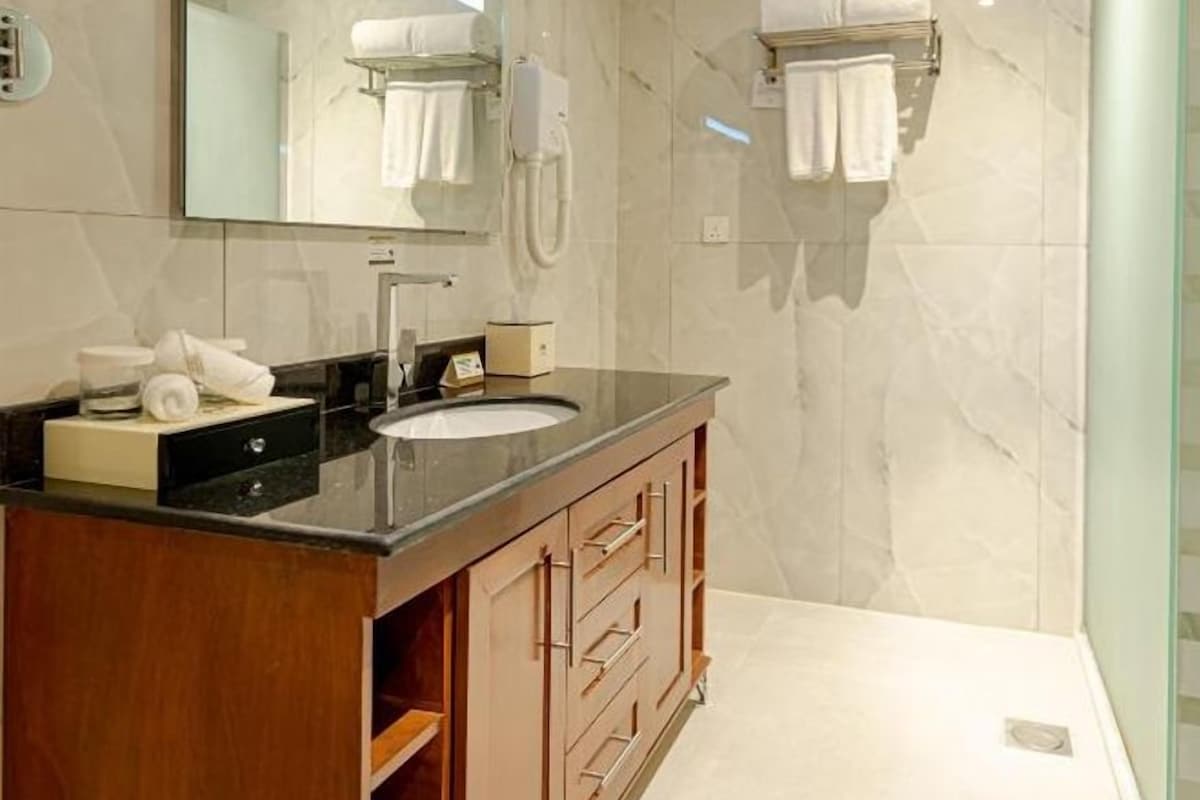 Un baño moderno con lavamanos de mármol, tocador de madera y cabina de ducha de vidrio.