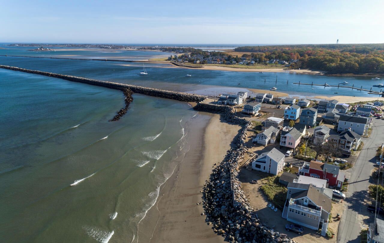 An aerial view of a coastal town with a beach, houses, and a breakwater.