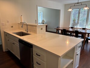 A kitchen with a white countertop, a dishwasher, and a dining area with a table and chairs.