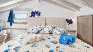 Une chambre avec un plafond en pente, un lit recouvert d’une literie à motifs, deux décorations murales en forme de corail et une fenêtre offrant une vue.
