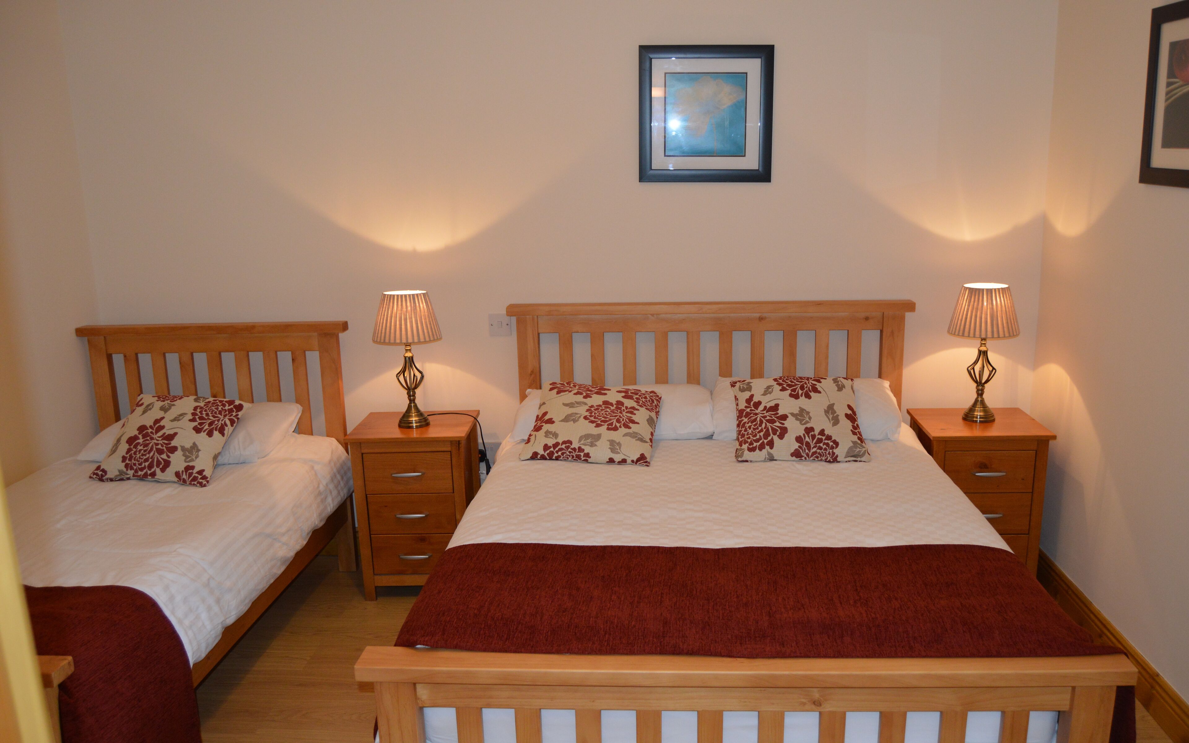 Habitación doble con dos camas individuales, cada una con cabecero de madera, mesitas de noche y lámparas. En la pared, sobre las camas, hay un cuadro enmarcado.