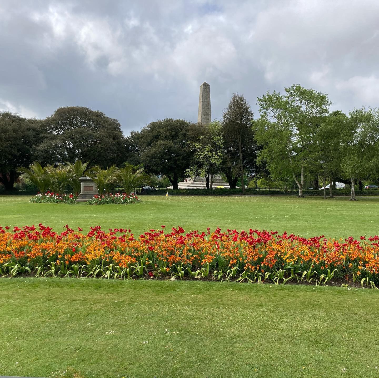 A park with a monument, green lawns, and flower beds.