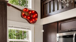 Una cocina con una guitarra roja colgada en la pared, un refrigerador de acero inoxidable y armarios de madera.