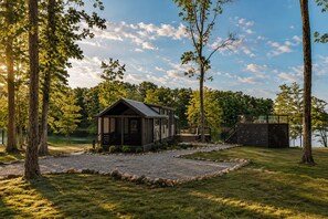 A cabin with a porch, a deck, and a staircase leading to a platform overlooking a body of water. - The Dolly House at The Retreat at Water's Edge (Tracy City)