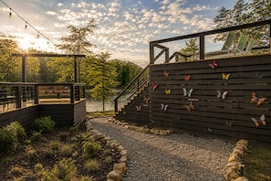A wooden deck with a staircase leading to a covered area, surrounded by a garden with a pebble path.