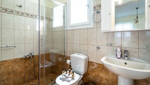 Een badkamer met een douchecabine van glas, een toilet, een wastafel en een spiegel boven de wastafel.