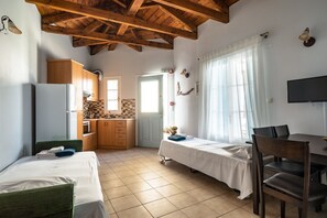 A room with two beds, a dining table, a TV, wooden cabinets, a kitchen area, and a window with curtains.