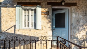 Un edificio in pietra con una porta bianca, una finestra con persiane e una ringhiera in metallo.