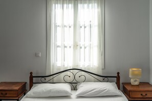 Un lit avec du linge de lit blanc, une tête de lit en bois et une table de chevet avec une lampe.