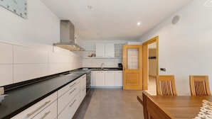 Een moderne keuken met witte kasten, een zwart aanrecht en een houten eettafel met stoelen.