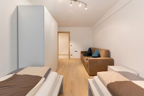 A modern hotel room with a bed, a sofa, a small table, and a wardrobe. - 'Apartment Bergkristall' with Mountain View, Garden & Wi-Fi (Nova Levante)