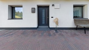 Een modern gebouw met een donkere deur, twee ramen, een bankje en een klein sculptuur.