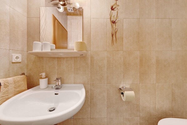 Un baño con lavamanos, espejo, toallero y soporte para papel higiénico.