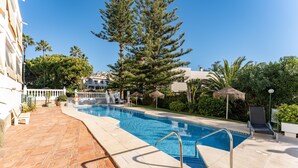 Une piscine avec une terrasse carrelée, un fauteuil de relaxation et un grand arbre.