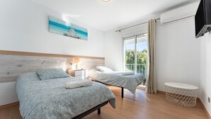 Une chambre avec deux lits, une table de chevet, une lampe, un téléviseur et une fenêtre avec des rideaux.