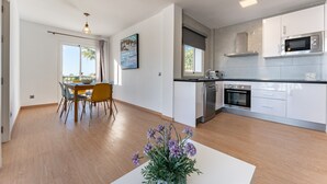 Une cuisine moderne avec des meubles blancs, un four à micro-ondes en acier inoxydable et un coin repas comprenant une table et des chaises.