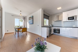 Uma cozinha moderna com armários brancos, micro-ondas de aço inoxidável e um espaço de refeições com mesa e cadeiras.