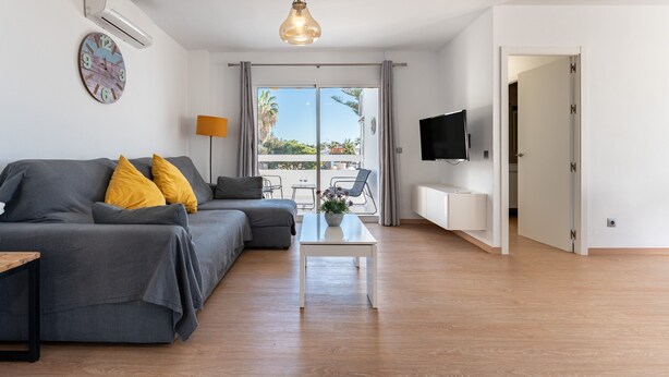 Un salon moderne avec un canapé, une table basse, un téléviseur et une vue à travers une porte vitrée.