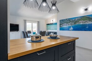 A modern kitchen with a wooden countertop, black cabinets, and a large painting of a coastal scene.