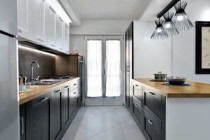 A modern kitchen with dark cabinetry, a wooden countertop, stainless steel appliances, and a unique pendant light.