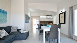 A modern living room with a grey sectional sofa, a dining table with chairs, and a kitchen in the background. - Appartamento Vista Golfo with Sea View, Terrace & Wi-Fi (Cala Gonone)