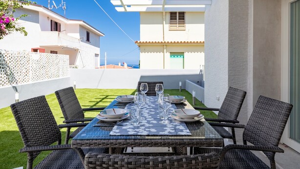 A patio with a table set for four, surrounded by wicker chairs, under a pergola. - Appartamento Prato al Mare with Garden, A/C & Wi-Fi (Cala Gonone)