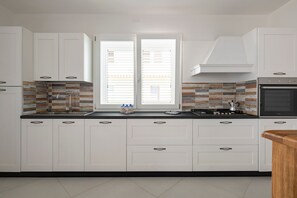 Une cuisine moderne avec des meubles blancs, un plan de travail noir, une cuisinière et une fenêtre avec des stores.