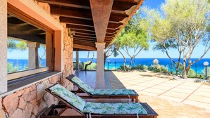 Un espacio de estar al aire libre cubierto con sillones reclinables, un muro de piedra y vistas al mar.