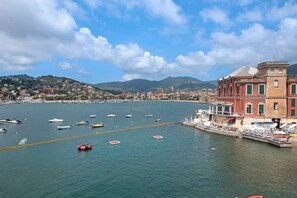 Un pueblo costero con barcos amarrados en el muelle, edificios de fachadas rojas y verdes, y montañas al fondo.