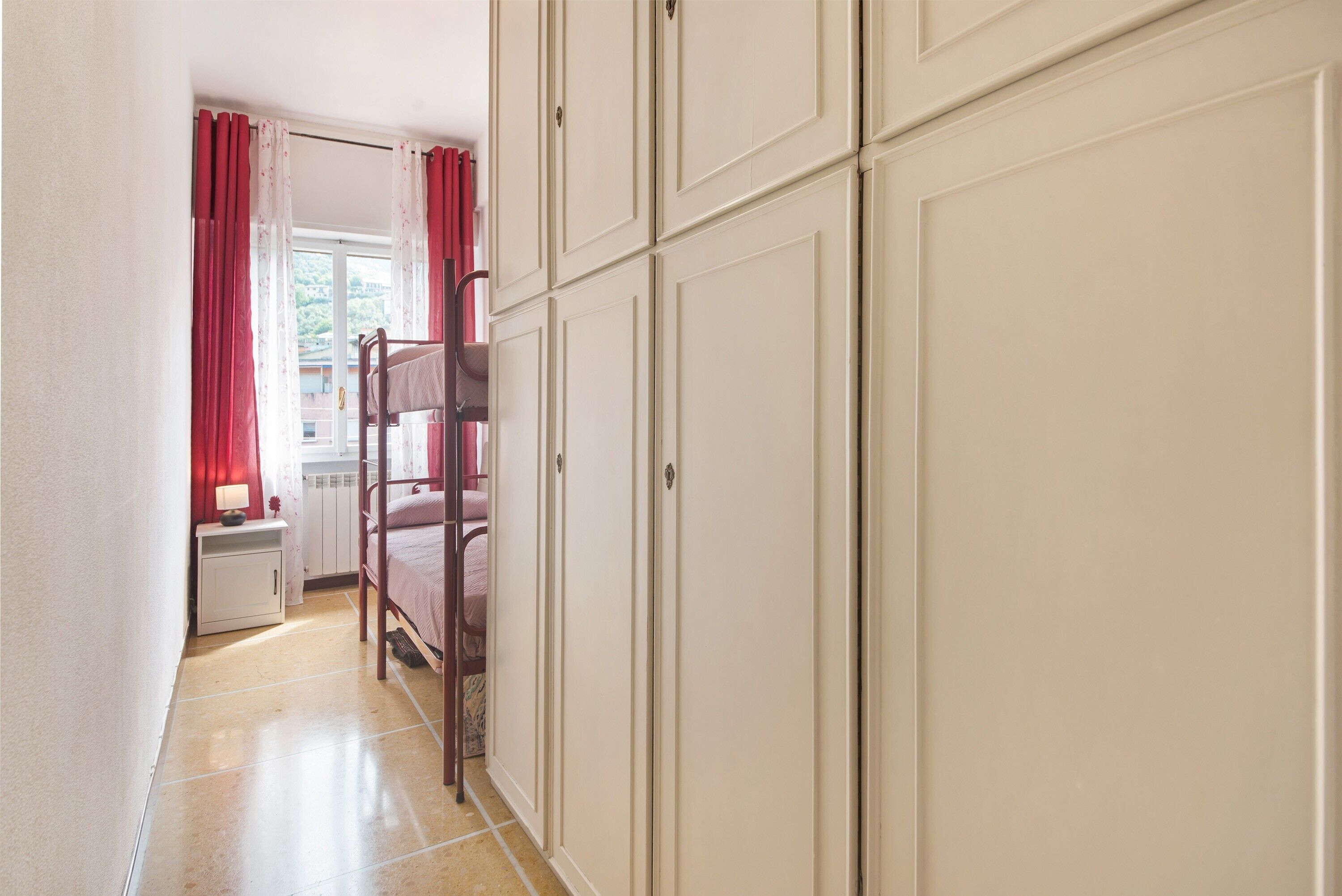 A narrow hallway with a bunk bed, a white cabinet, and a door leading to a room with a window.