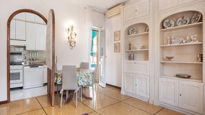 Una cocina con armarios blancos, una mesa de comedor con sillas, y un pasillo con un espejo y estanterías.