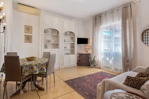 Un coin repas avec une table dressée pour quatre personnes, un canapé, un téléviseur et une fenêtre avec des rideaux.