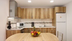 Una cocina moderna con armarios de madera, un refrigerador blanco, un microondas y un frutero sobre la mesa.