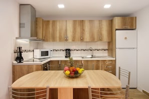 Una cocina moderna con armarios de madera, un refrigerador blanco, un microondas y un frutero sobre la mesa.