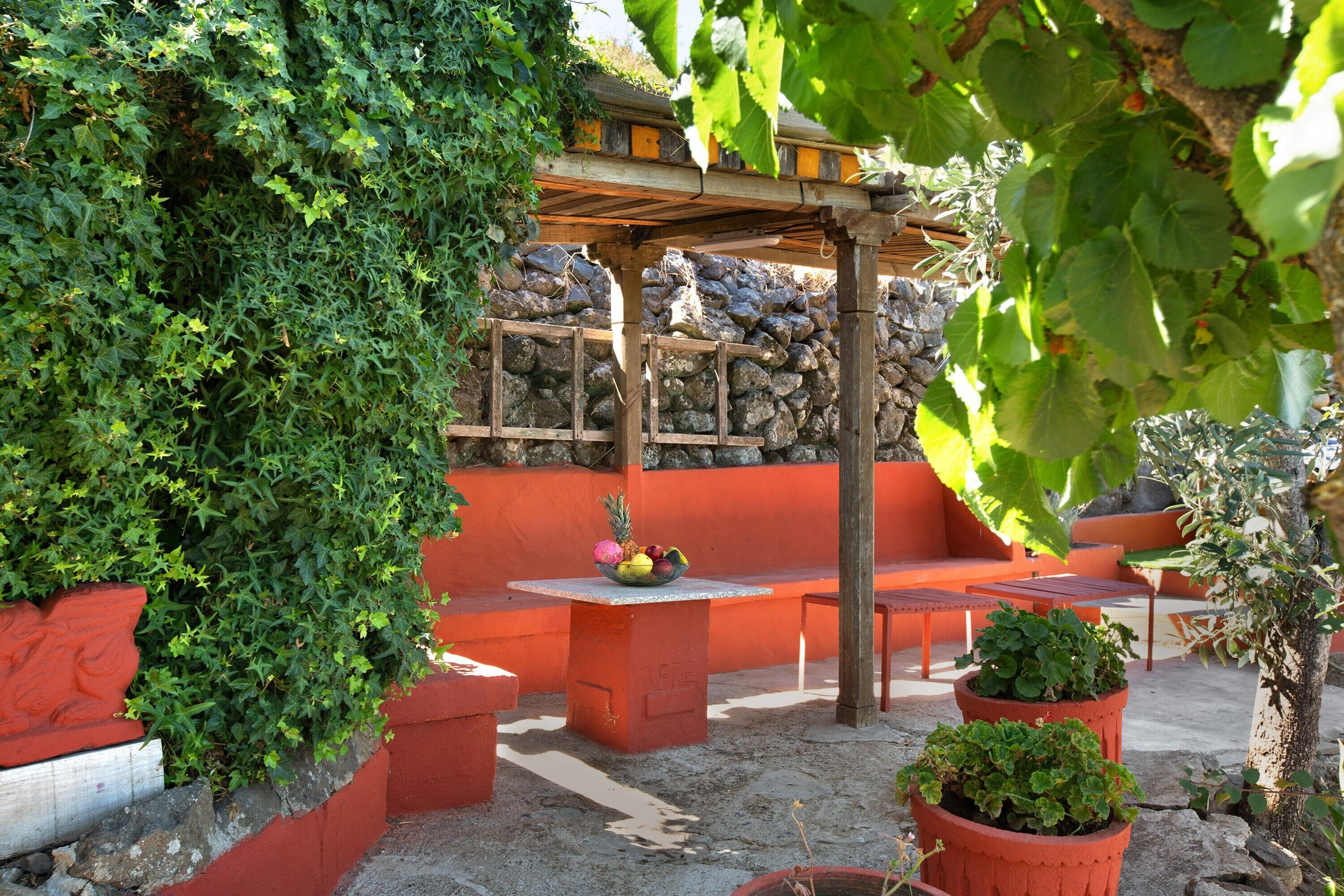 Un espace patio agrémenté d’un mur en pierre, de bancs en bois et de plantes en pot.