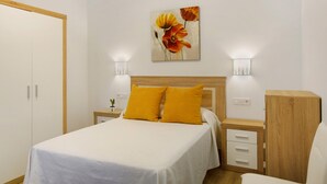 Un dormitorio con una cama, dos lámparas de noche, una mesita de noche, un armario de madera y un cuadro colgado en la pared.