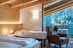 Une chambre dans un chalet en bois, avec deux lits, une chaise, une table de chevet et une fenêtre donnant sur une forêt.