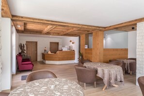 Ein Empfangsbereich mit einem Holzbüro, einem roten Sessel und einem Essbereich mit Tischen und Stühlen.