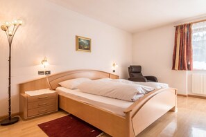 A bedroom with a bed, bedside tables, a floor lamp, a chair, a painting, and a window with curtains.