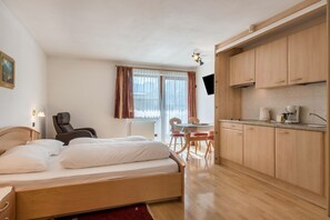 A bedroom with a single bed, a chair, a table, and a kitchenette.