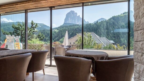 Un interior moderno con ventanas amplias, vistas a montañas y un patio con mobiliario exterior.