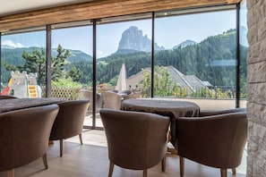 Interior moderno com grandes janelas, vista para montanhas e um espaço de varanda com mobiliário para área externa.