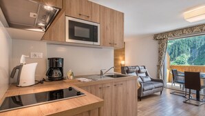Una cocina moderna con microondas integrado, cafetera y hervidor. Hay una zona de comedor con mesa y sillas.
