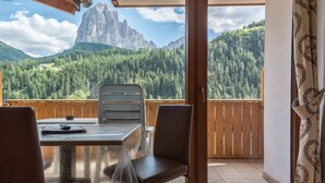 Un balcón con mesa y sillas, baranda de madera y vista a un paisaje montañoso.