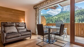 Una habitación con pared de madera, un sofá, una mesa de comedor con sillas y un amplio ventanal corredero con vista a la montaña.