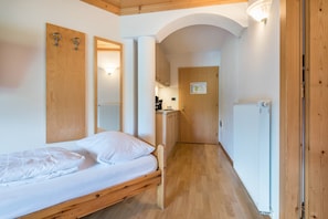 A room with a wooden bed, a mirror, a radiator, and a door leading to a kitchen area.