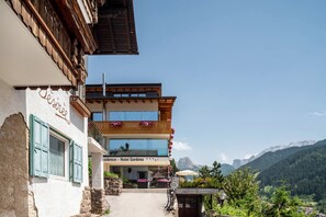 A hotel with a balcony, a sign reading 'Hotel Gardena,' and a mountain view in the background.