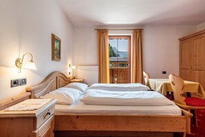 A wooden bed with two pillows, a nightstand, a lamp, a window with curtains, and a view of a mountain.