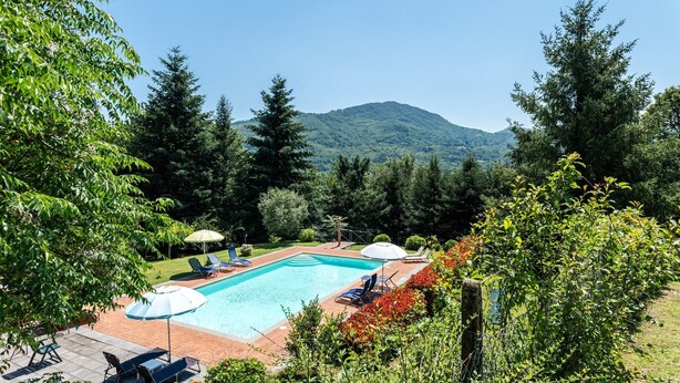 A rectangular swimming pool with lounge chairs and umbrellas, surrounded by trees and a mountain in the background. - Villa 'Rifugio Arcobaleno' with Mountain View, Heated Pool & Wi-Fi (Popiglio)