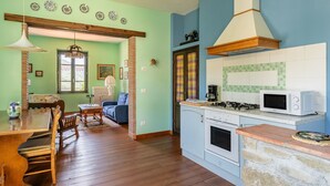 A kitchen with a stove, microwave, and a dining area with a table and chairs. - Villa 'Rifugio Arcobaleno' with Mountain View, Heated Pool & Wi-Fi (Popiglio)